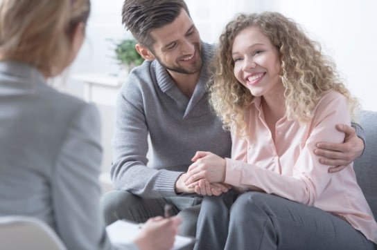 couple in therapy session smiling, man with arm around woman