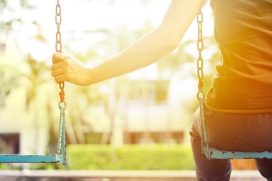close up of person sitting on swing holding onto chain of empty swing next to them