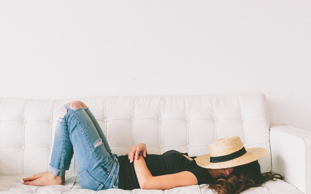 woman lying on sofa with hat over face