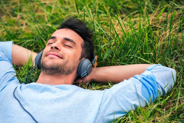 man laying in grass wearing headphones looking relaxed
