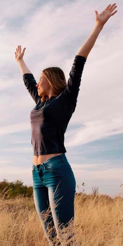 woman in field with arms reaching up to sky