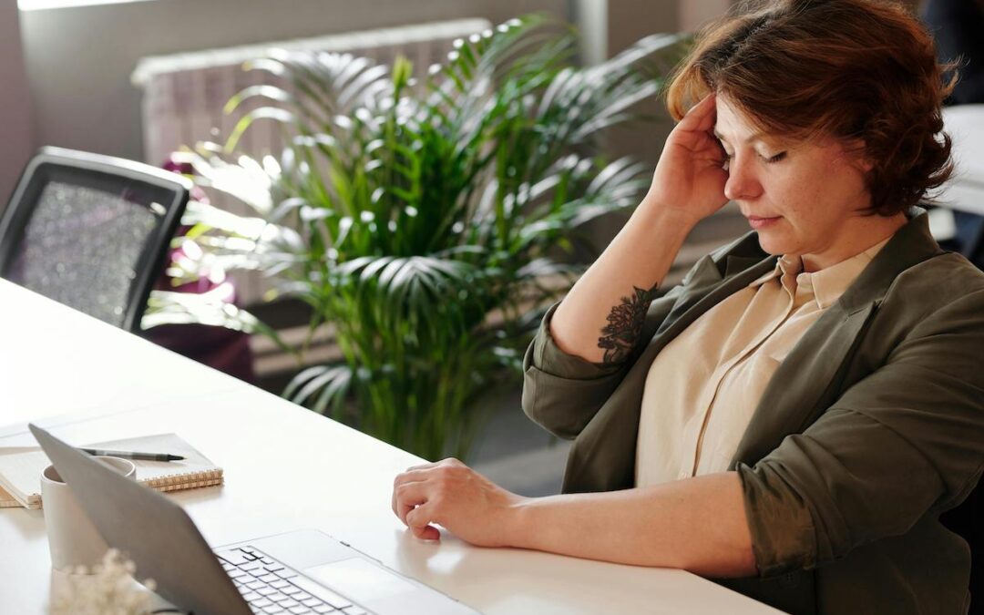 woman at work with hand on temple and eyes closed