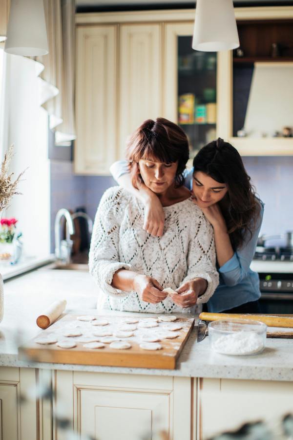 young woman with arm around mother affectionately while they bake cookies together