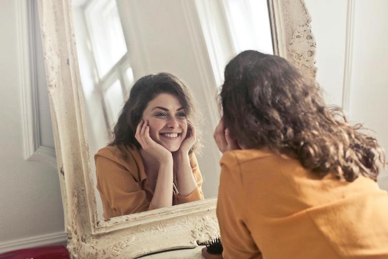 woman smiling at her reflection in mirror