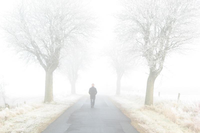 man walking down road in winter mist