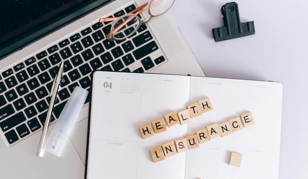 laptop and notebook with scrabble letters spelling health insurance