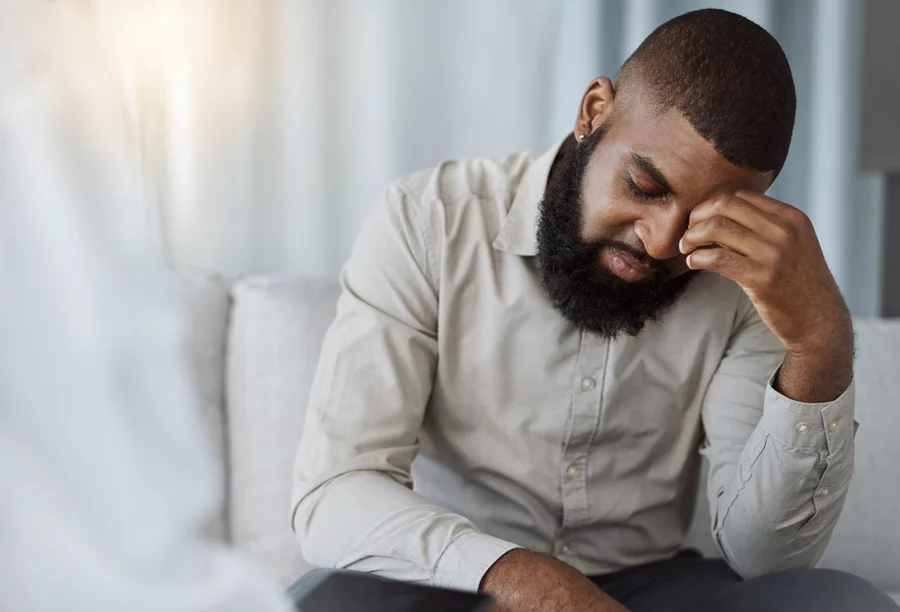 Black patient with head down and eyes closed in therapy office, showing stress and worry as he wonders, does anxiety get worse before it gets better?