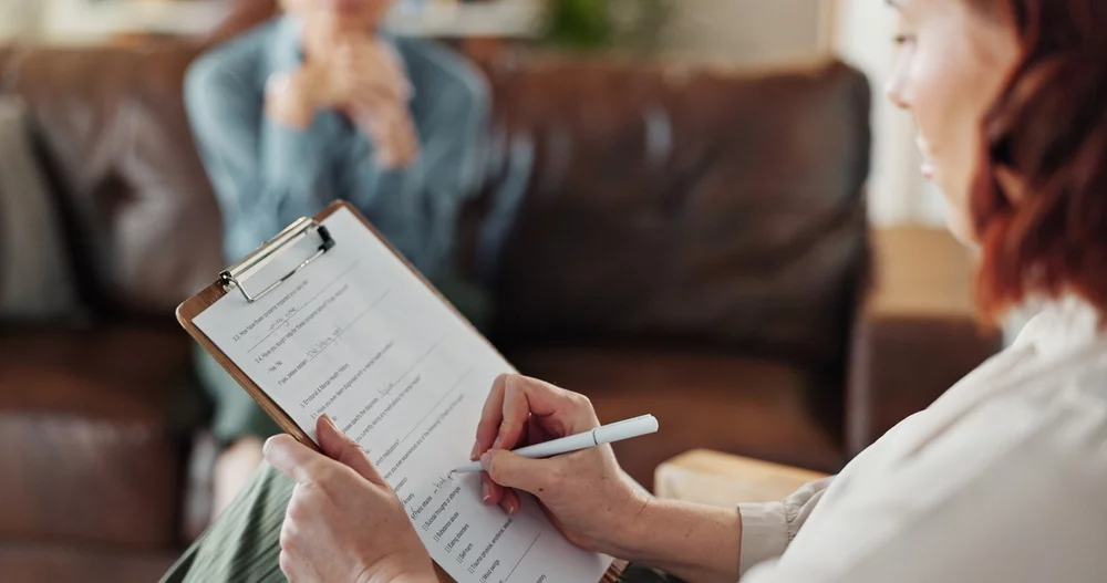 Therapist reviewing intake form on clipboard with client on couch, discussing limits of insurance for therapy and options for private payment.